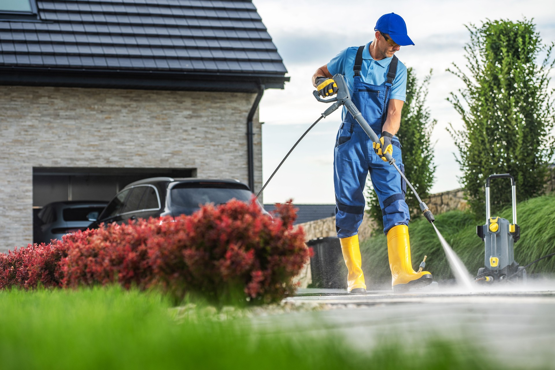 Man Using a Pressure Washer to Clean Driveway While Standing on a Sunny Afternoon